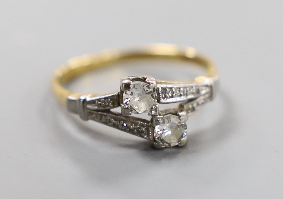 An 18ct, plat and two stone diamond crossover ring, with diamond set shoulders, size N/O, gross weight 2.7 grams.